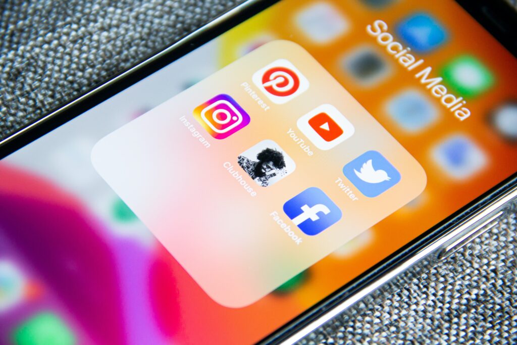 An IPhone with a social media folder with the following apps: Pinterest, Youtube, Twitter, Instagram, Clubhouse, Facebook