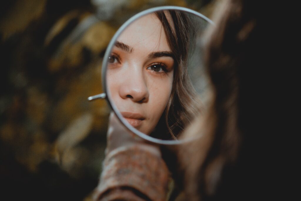 Girl holding a small circular mirror and looking at herself.