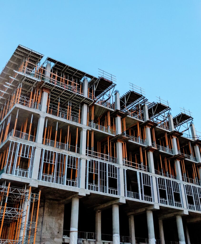 construction site with a four story building that is being constructed. There are lots of orange support beams to keep the building steady.